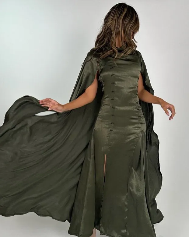 Olive satin dress with a long flowing cape, caught in motion