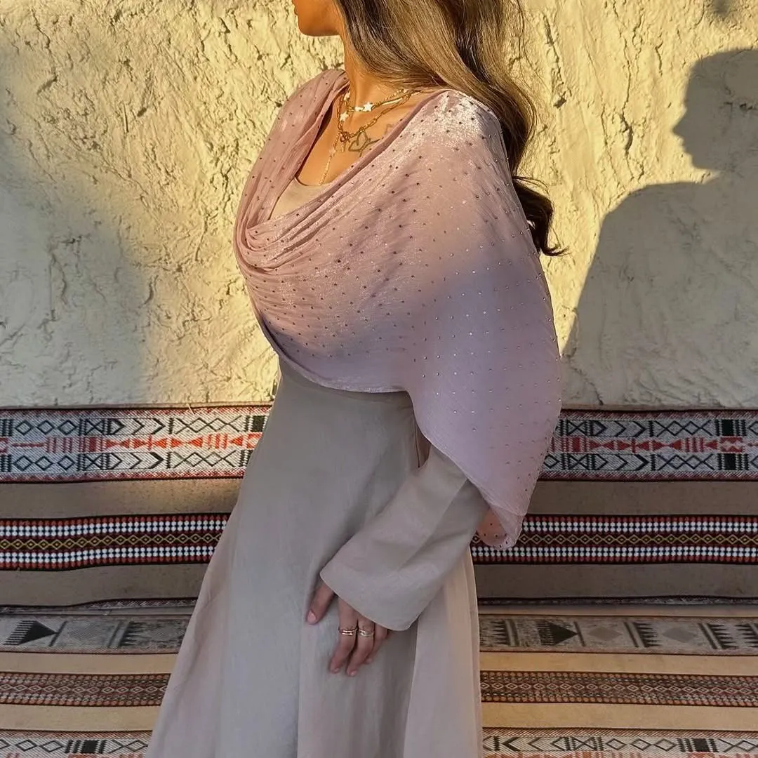 Blush shimmer drape over a stone-coloured long dress, beside a woven cushion